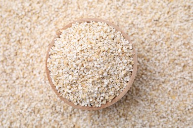 Wooden bowl on raw barley groats, top view