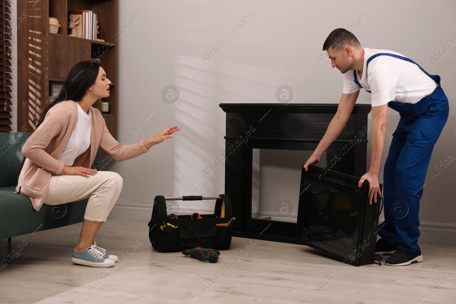 Photo of Young woman and professional technician with electric fireplace in room. Installing heater