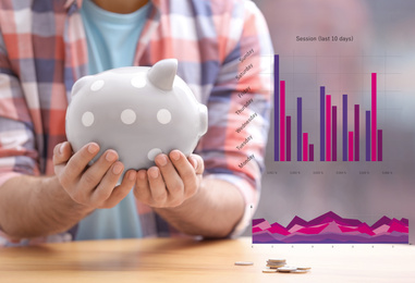 Man with piggy bank and graphs on blurred background, closeup