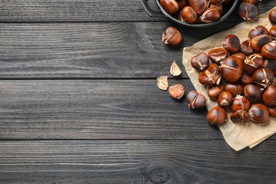 Photo of Tasty roasted edible chestnuts on black wooden table, flat lay. Space for text