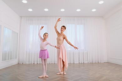 Photo of Little ballerina and her teacher practicing dance moves in studio. Space for text
