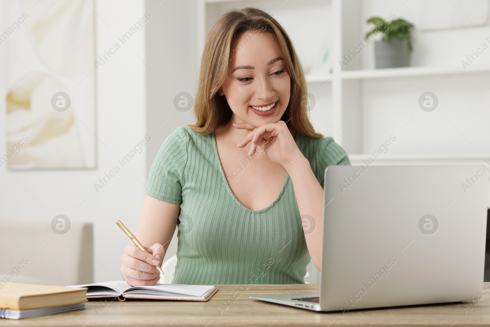 Photo of Young woman having video chat via laptop at wooden table indoors