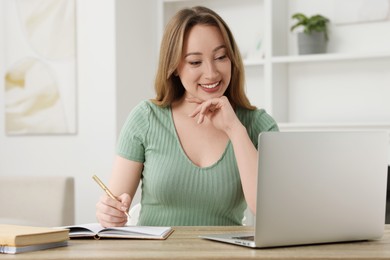 Young woman having video chat via laptop at wooden table indoors