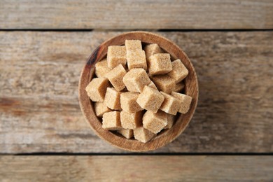 Photo of Bowl with brown sugar cubes on wooden table, top view