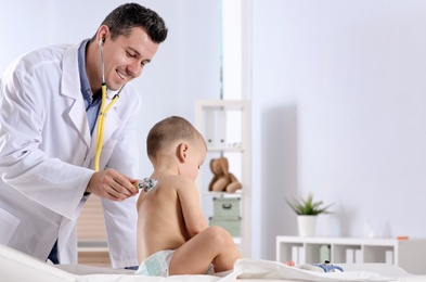 Photo of Children's doctor examining little boy with stethoscope in hospital. Space for text