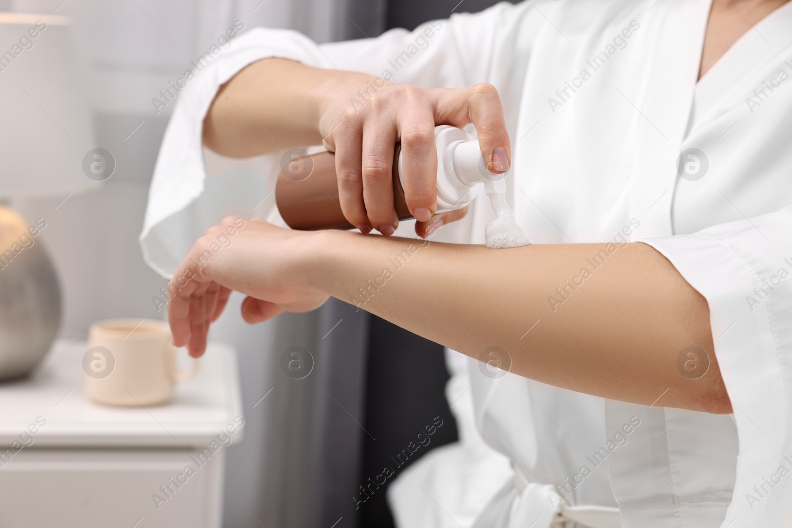 Photo of Woman applying self-tanning product onto arm indoors, closeup