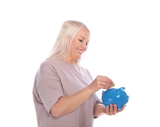 Mature woman putting money into piggy bank on white background