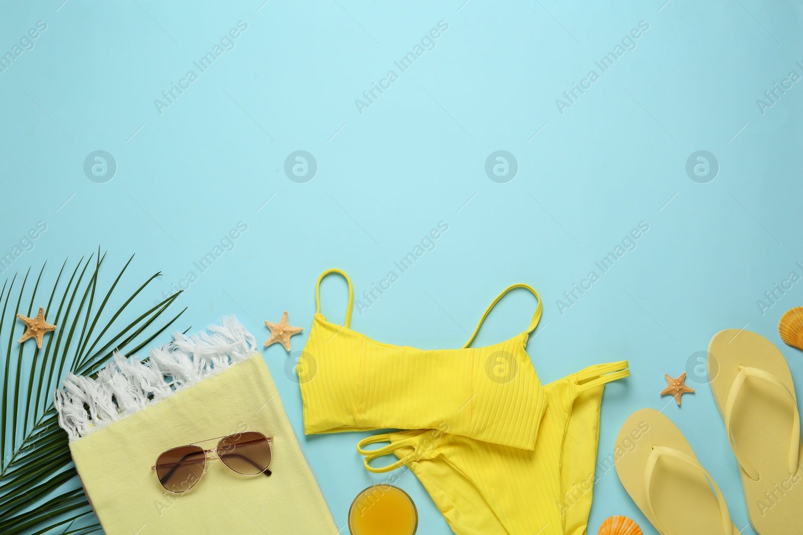 Photo of Beach towel, swimsuit, flip flops and sunglasses on light blue background, flat lay. Space for text