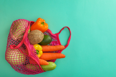 Photo of Net bag with fruits and vegetables on turquoise background, top view. Space for text