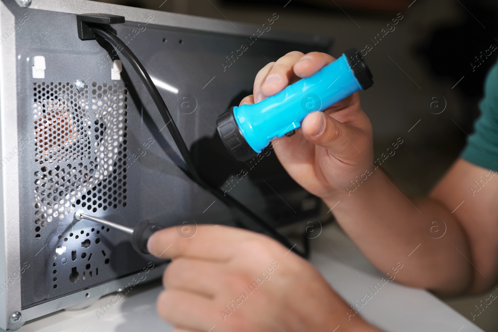 Photo of Repairman with flashlight fixing microwave oven indoors, closeup