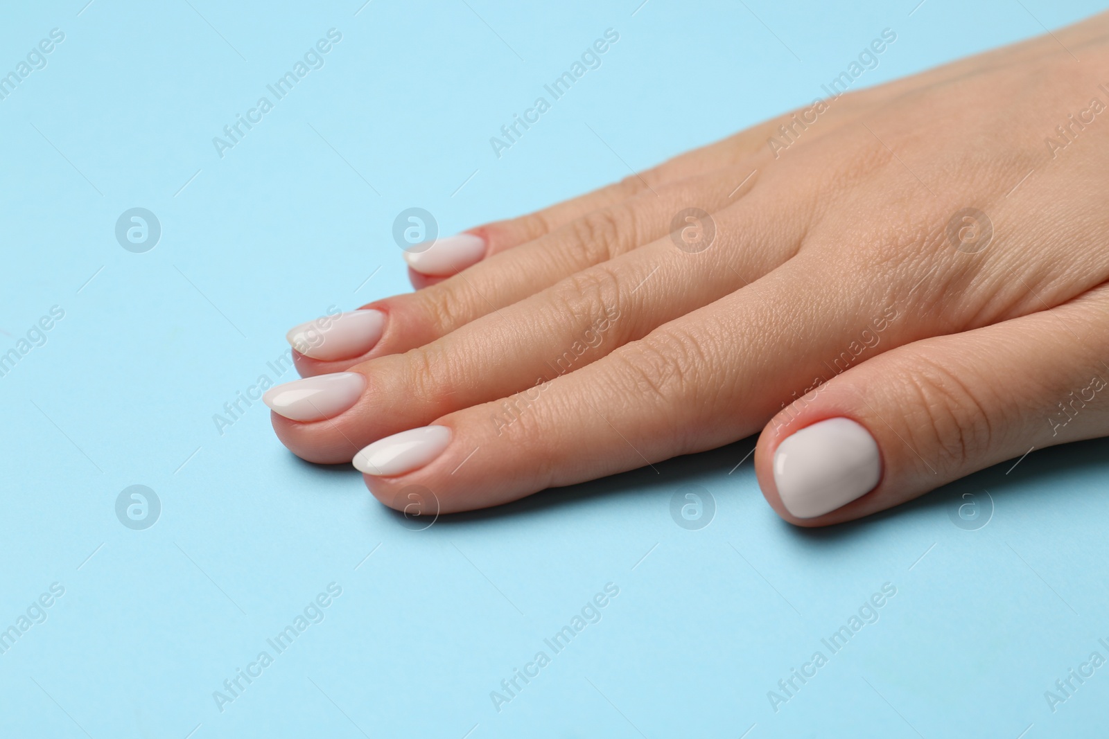 Photo of Woman showing her manicured hand with white nail polish on light blue background, closeup