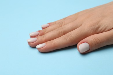 Woman showing her manicured hand with white nail polish on light blue background, closeup