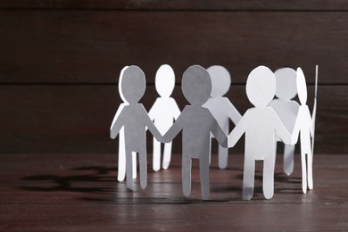 Photo of Teamwork concept. Paper figures of people holding hands on wooden table, closeup and space for text
