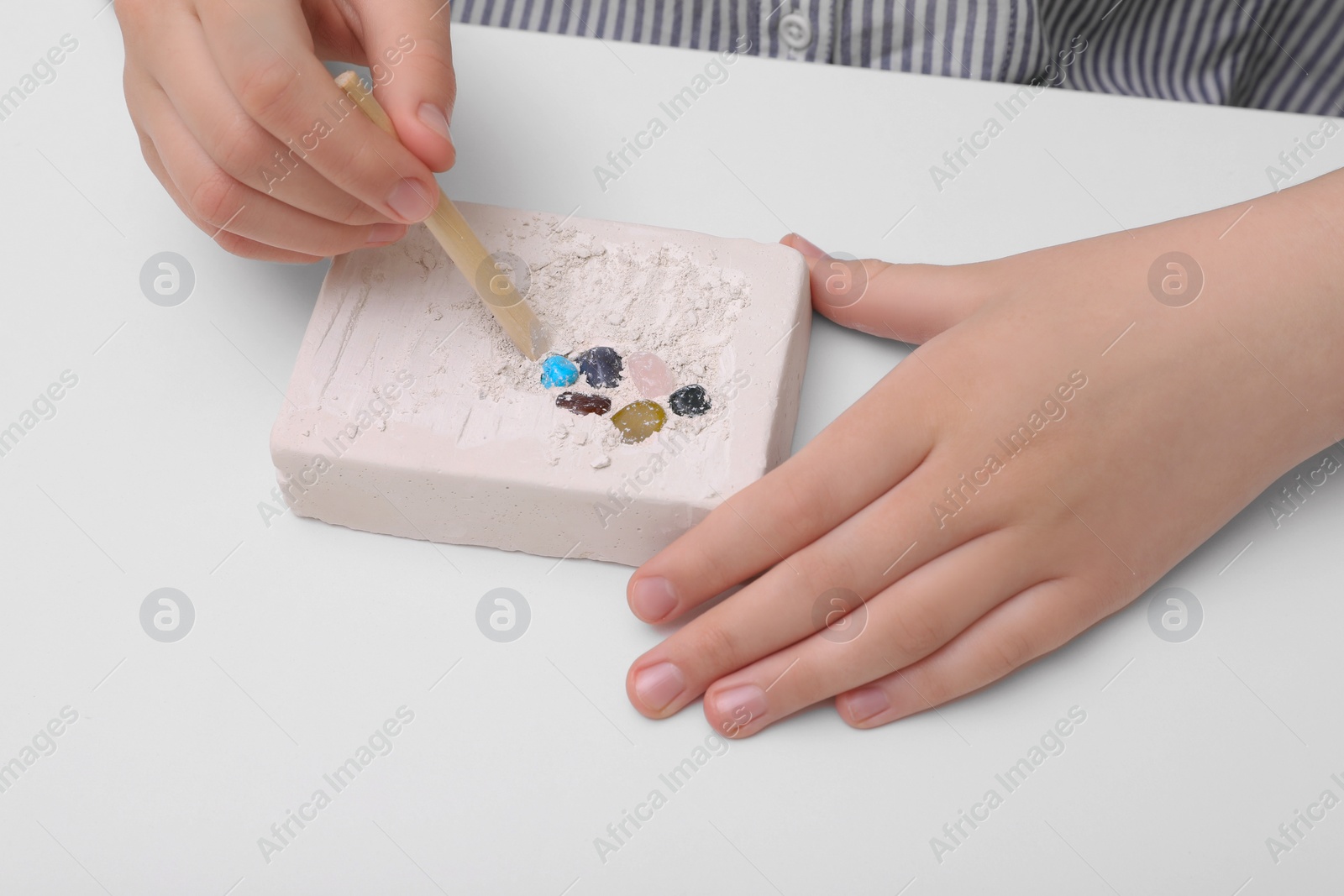 Photo of Child playing with Excavation kit at white table, closeup. Educational toy for motor skills