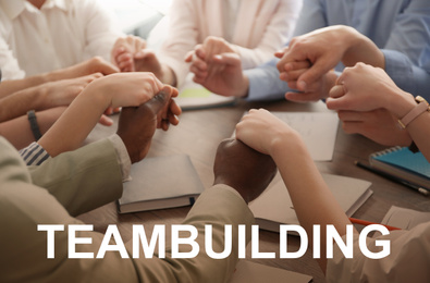 Image of People holding hands together at table and text TEAMBUILDING