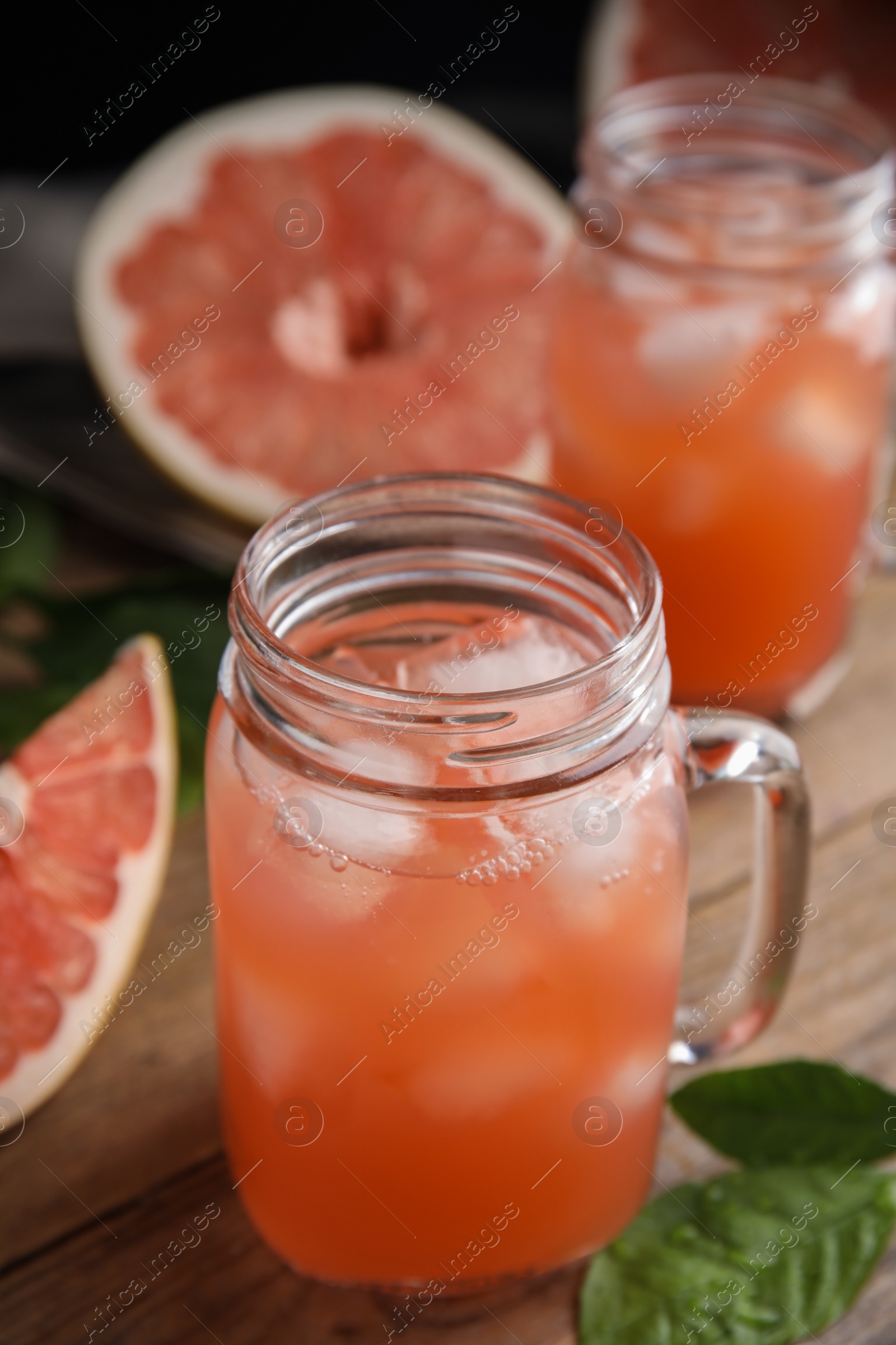 Photo of Glass jar with cold pomelo juice and leaves on wooden table