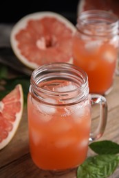 Glass jar with cold pomelo juice and leaves on wooden table