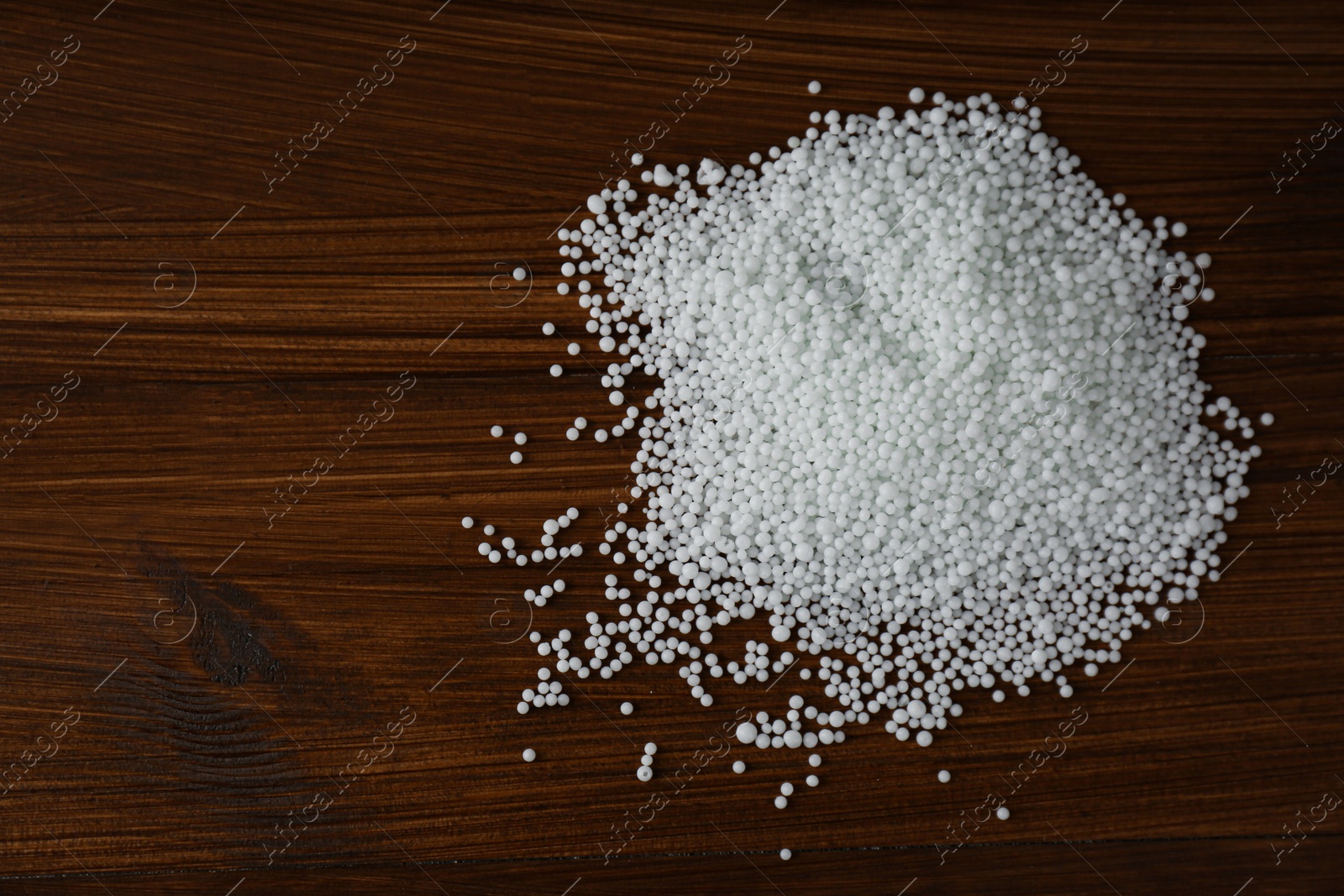 Photo of Pellets of ammonium nitrate on wooden table, flat lay with space for text. Mineral fertilizer