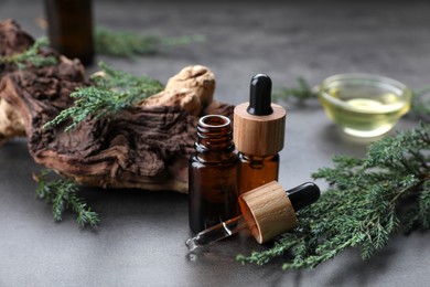 Bottles of juniper essential oil and twigs on grey table