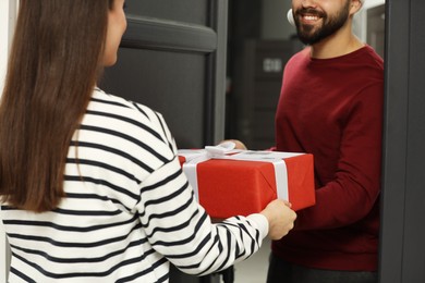 Photo of Courier giving young woman Christmas gift box indoors, closeup. Sending present by mail