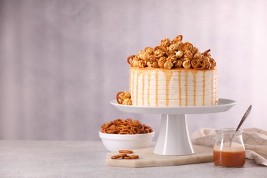 Photo of Caramel drip cake decorated with popcorn and pretzels on light table, space for text