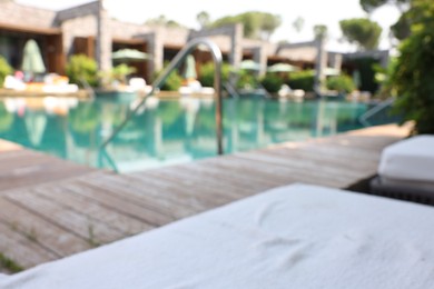 Photo of Outdoor swimming pool with wooden deck and sun loungers, blurred view. Luxury resort
