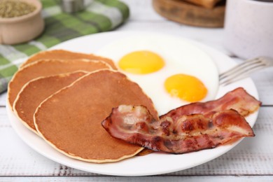 Photo of Tasty pancakes with fried eggs and bacon on white wooden table, closeup