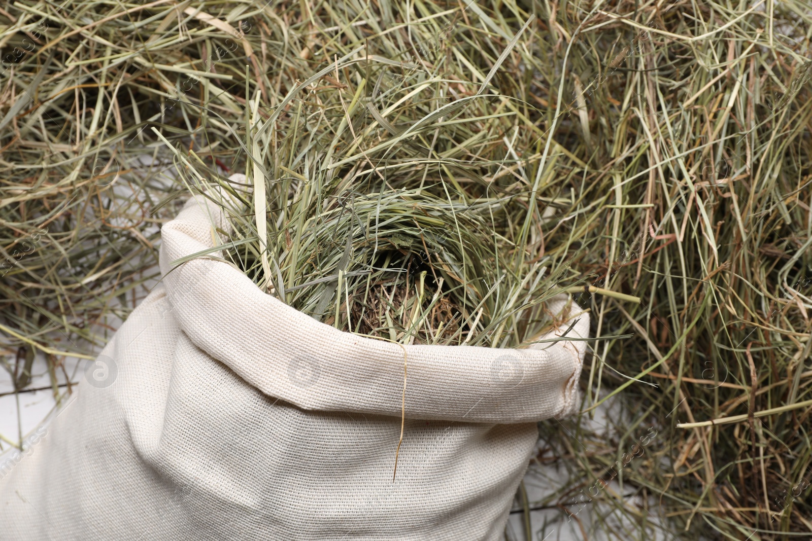 Photo of Burlap sack with dried hay on white wooden table, closeup