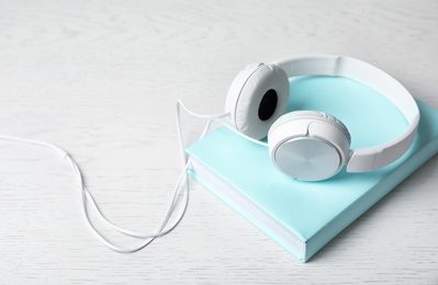 Photo of Modern headphones with hardcover book on wooden background. Space for text