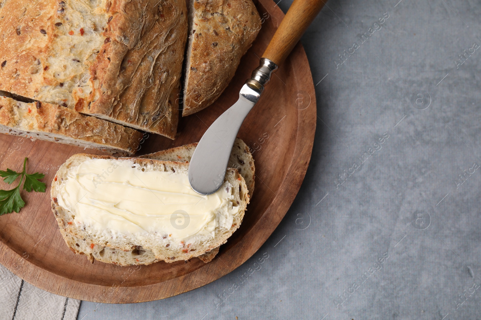 Photo of Tasty bread with butter and knife on grey textured table, top view. Space for text
