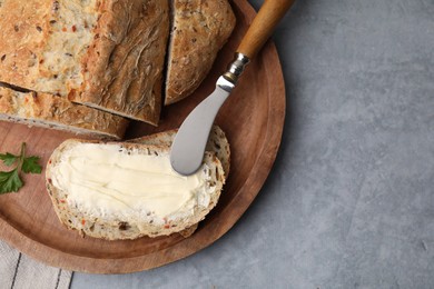 Tasty bread with butter and knife on grey textured table, top view. Space for text