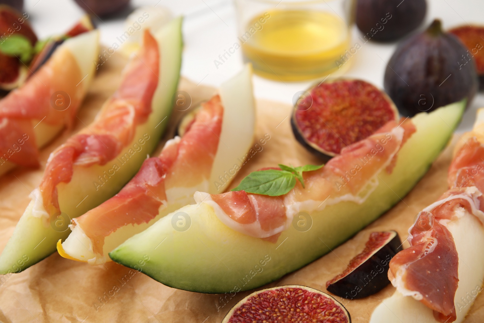 Photo of Tasty melon, jamon and figs served on parchment, closeup