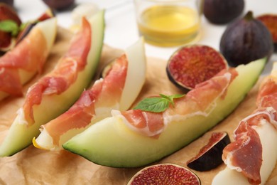 Photo of Tasty melon, jamon and figs served on parchment, closeup