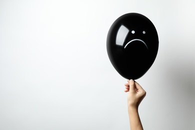 Woman holding balloon with sad face on white background, space for text. Threat of depression