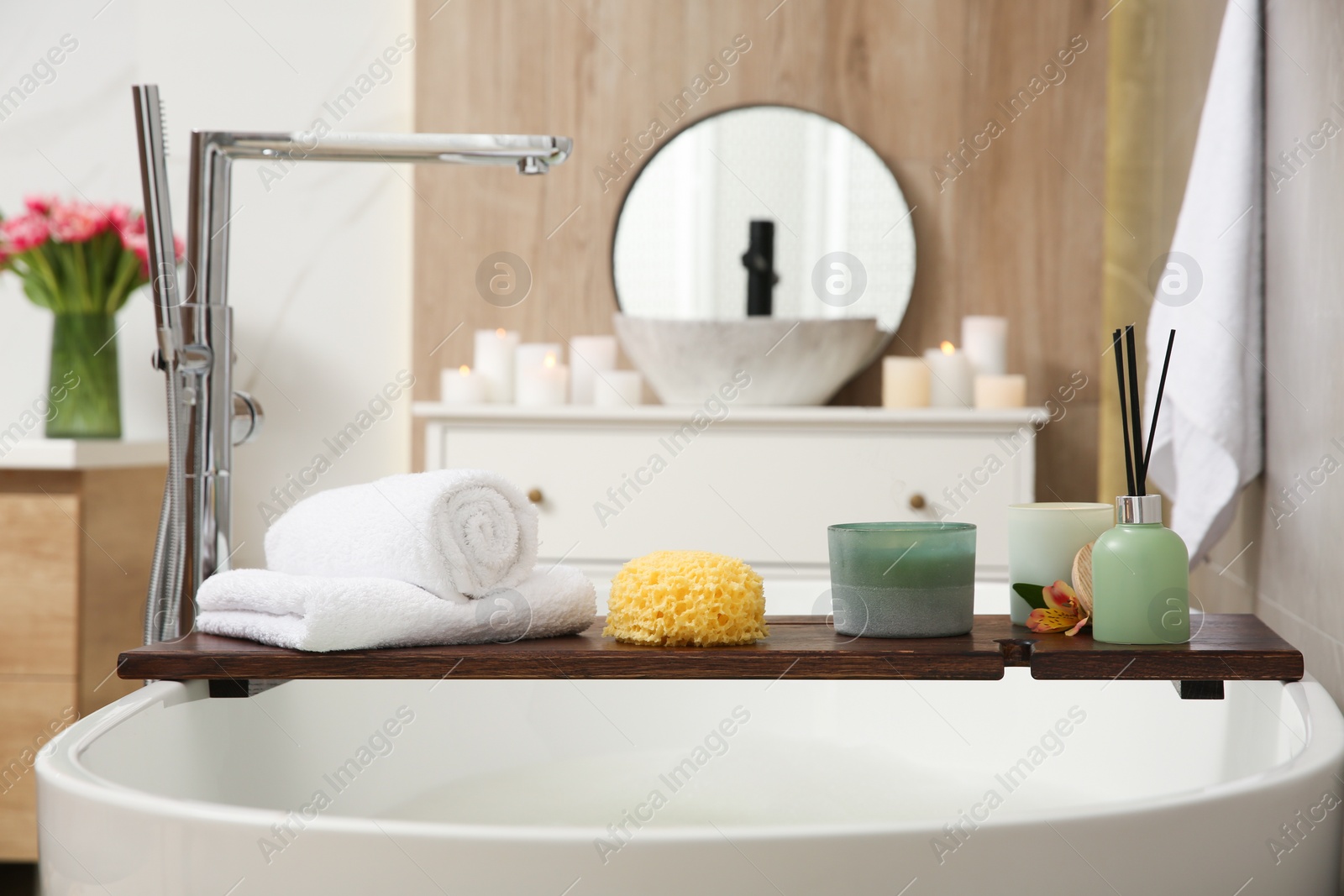 Photo of Wooden bath tray with candles, air freshener, towels and sponge on tub indoors