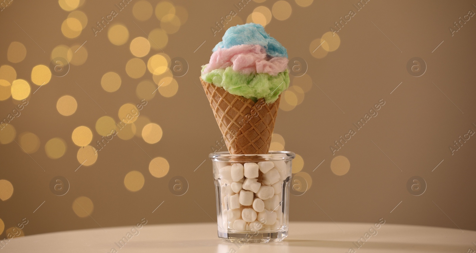 Photo of Sweet cotton candy in waffle cone on table against blurred lights