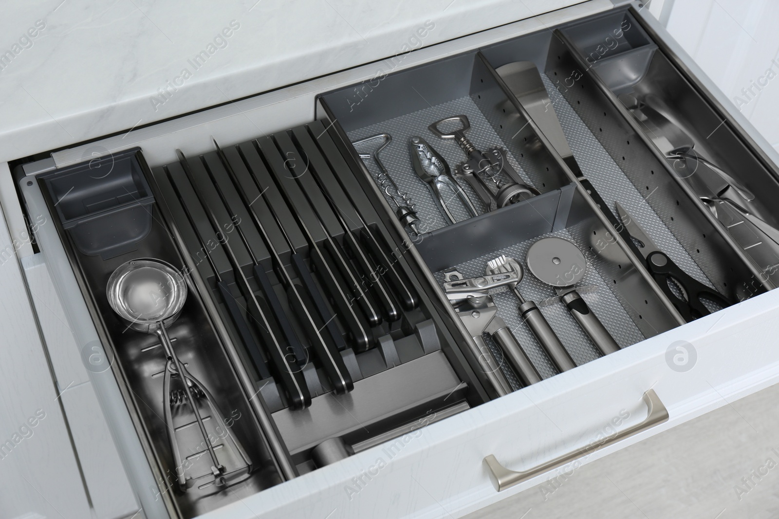 Photo of Open drawer with stainless steel utensil set, closeup. Order in kitchen
