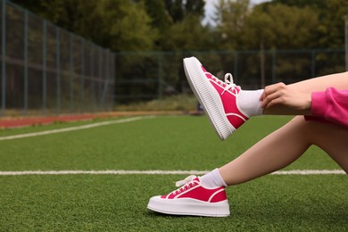 Photo of Woman wearing classic old school sneakers on green court outdoors, closeup. Space for text