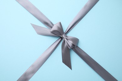 Photo of Grey satin ribbon with bow on light blue background, top view