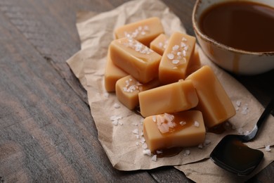 Photo of Delicious candies with sea salt and caramel sauce on wooden table, closeup. Space for text