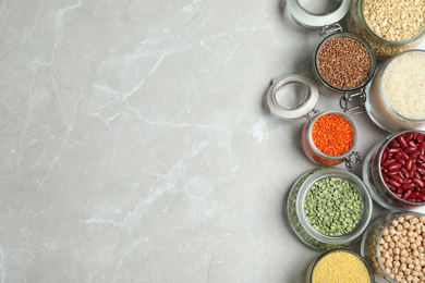 Flat lay composition with different types of legumes and cereals on grey marble table, space for text. Organic grains