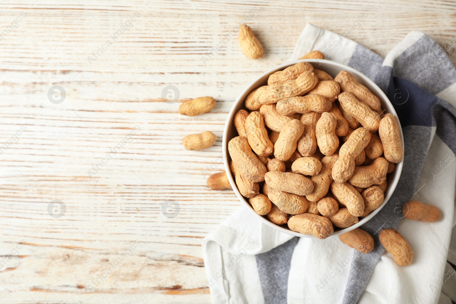 Photo of Bowl with peanuts in shell, napkin and space for text on wooden table, top view