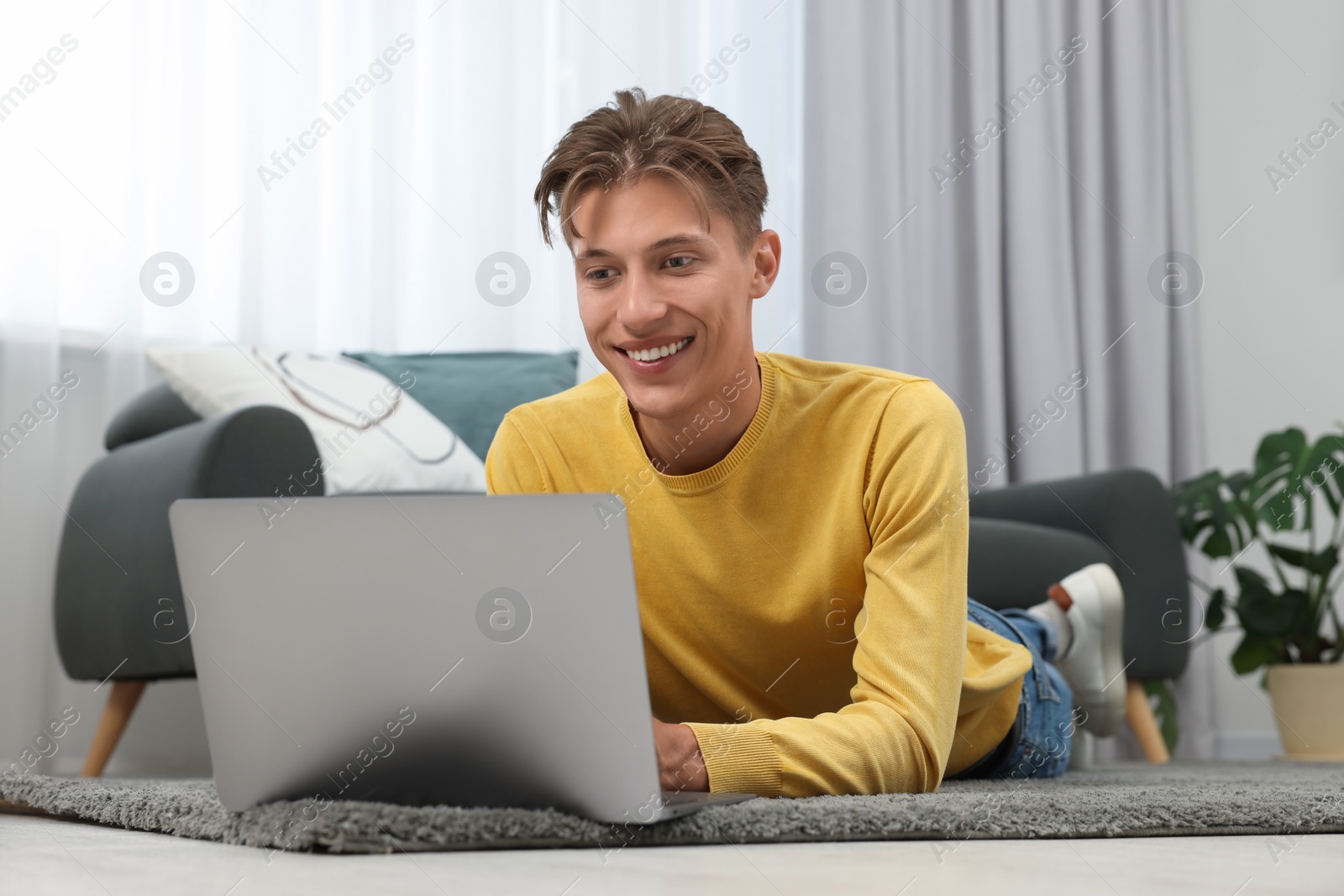 Photo of Happy young man having video chat via laptop on carpet indoors