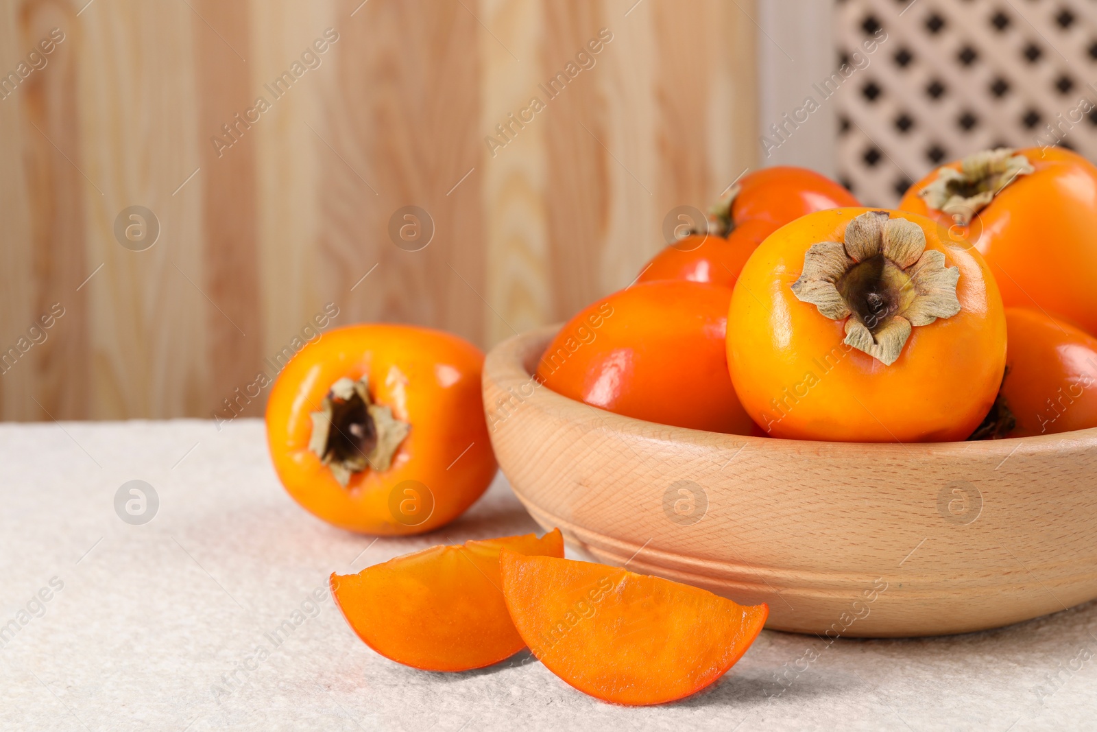 Photo of Delicious ripe persimmons on light textured table indoors, closeup. Space for text