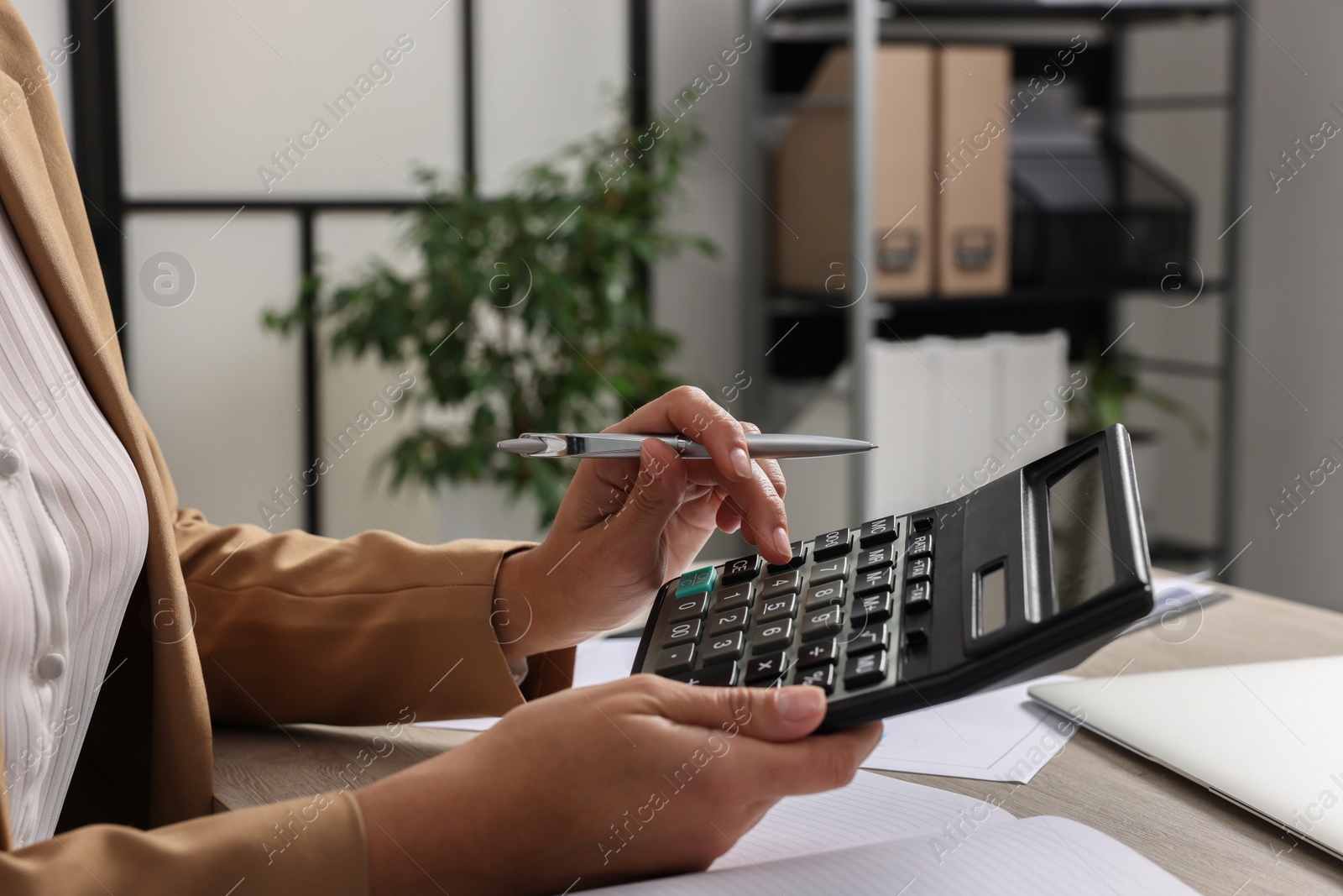 Photo of Woman using calculator at table in office, closeup