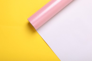 Roll of pink wrapping paper on yellow background, top view. Space for text