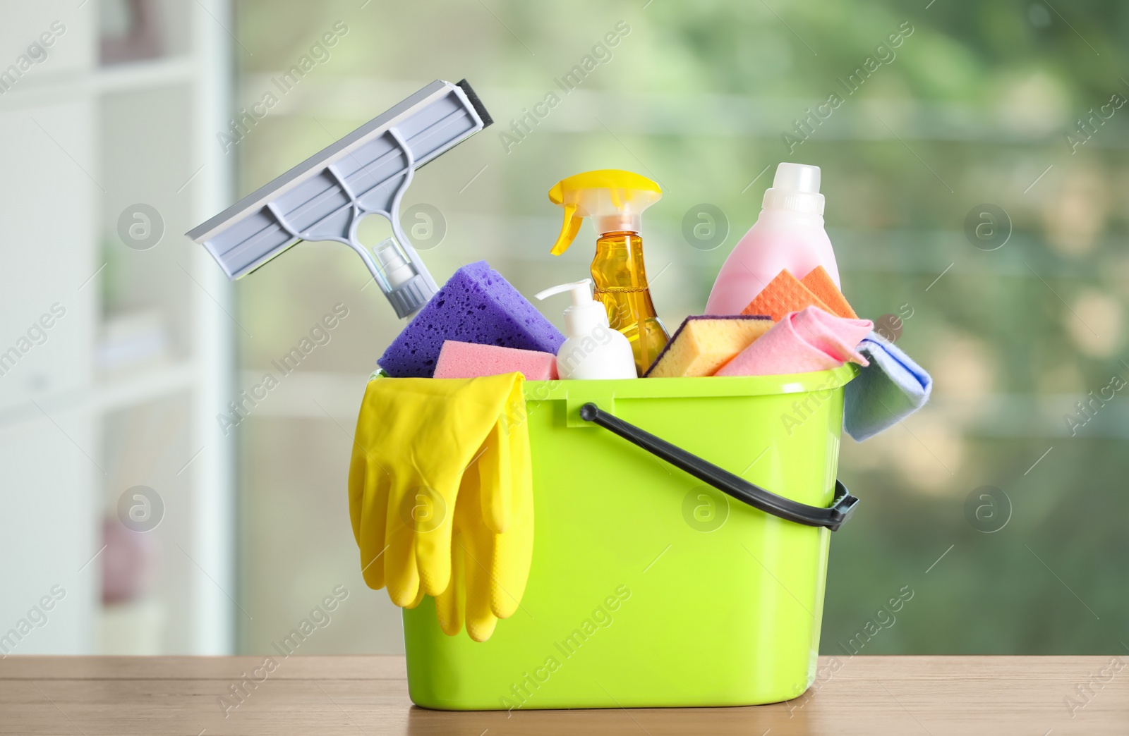 Photo of Light green bucket with cleaning products on wooden table indoors