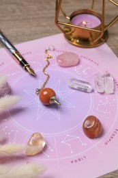 Astrology prediction. Zodiac wheel, gemstones, pendulum and burning candle on wooden table, closeup