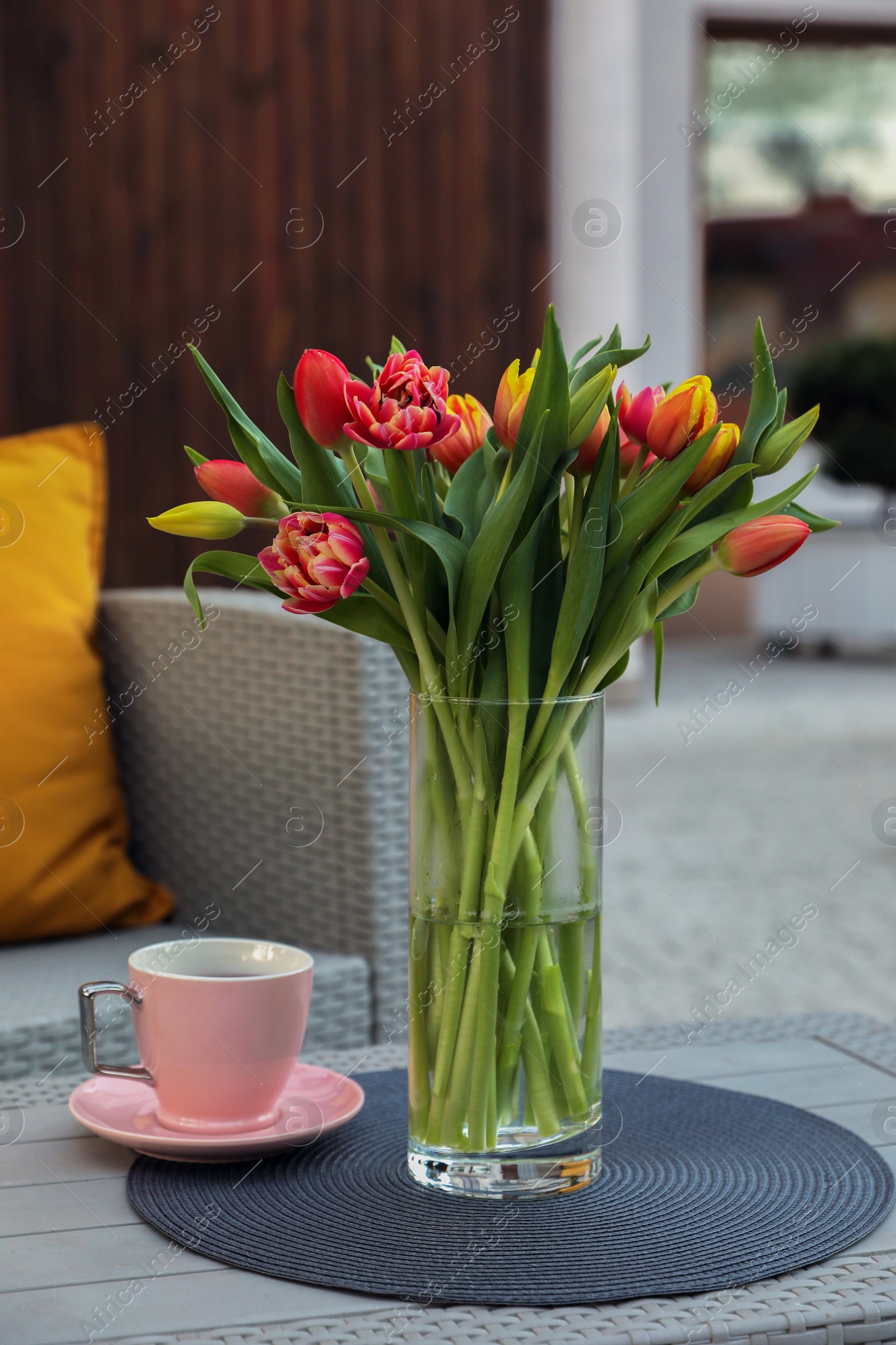 Photo of Beautiful bouquet of colorful tulips and cup with drink on rattan garden table outdoors