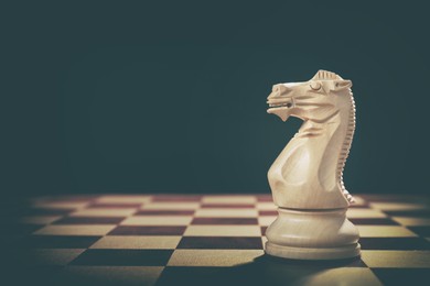 Image of Wooden knight on chessboard against dark background, space for text